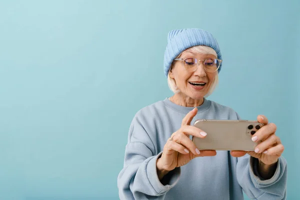 Увлекательная Пожилая Женщина Зимней Шляпе Очках Держащая Руках Телефон Смотрящая — стоковое фото