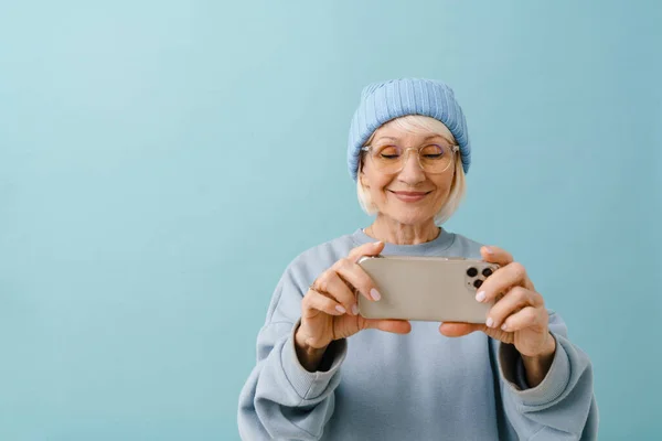 Улыбчивая Пожилая Женщина Зимней Шапке Очках Держа Руках Телефон Глядя — стоковое фото