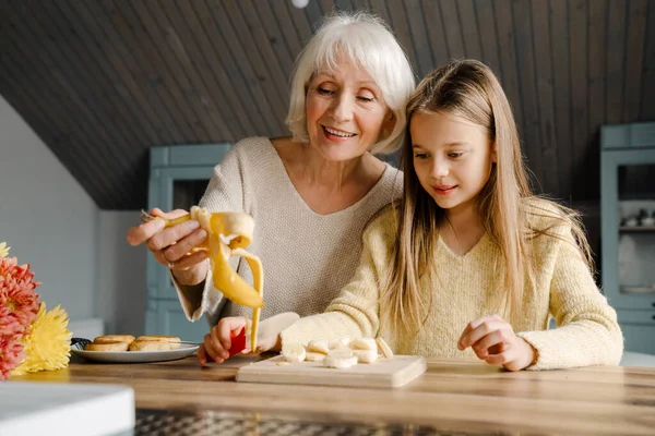 Stock image Happy grandmother and granddaughter cooking cheese pancakes together in kitchen at home