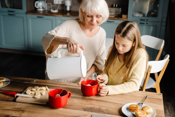 Happy grandmother and granddaughter cooking breakfast together in kitchen at home