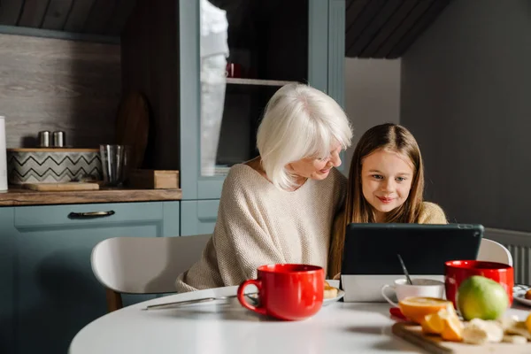 stock image Happy grandmother and granddaughter using tablet computer while having breakfast at home