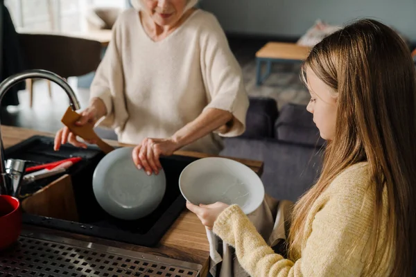 stock image Happy grandmother and granddaughter washing dishes together in kitchen at home