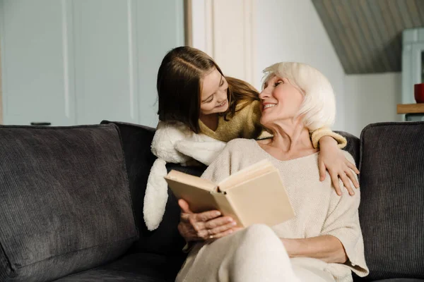 Šťastná Babička Mluví Svou Vnučkou Při Čtení Knihy Doma — Stock fotografie