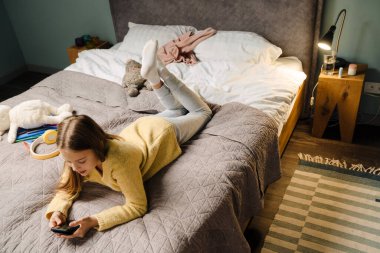 Beyaz mutlu kız evde yatarken cep telefonu kullanıyor.