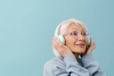 Gözlüklü ve kulaklıklı, mavi arka planda güzel bir son sınıf kadını.