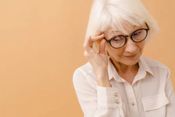 穿着白衬衫的漂亮老年妇女把眼镜调整到孤立的棕色背景上 — 图库照片