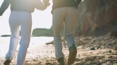 Neşeli bir çiftin el ele tutuşup deniz kenarında yürüdüğü arka manzara.