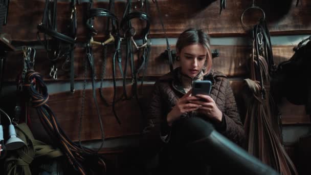 坐在马厩里时 专心致志的妇女骑手用手机发短信 — 图库视频影像