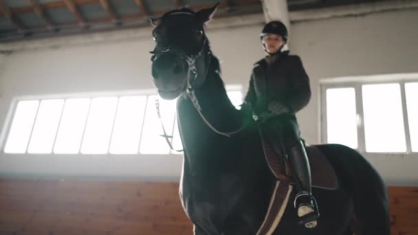 骑着头盔骑着马在马厩里看着她的积极女子骑手 — 图库视频影像