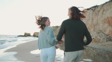 Sahilde koşan ve sarılan dost canlısı çiftin arka görüntüsü.