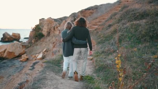 一对年轻貌美的夫妇在海边的斜坡上散步的背影 — 图库视频影像