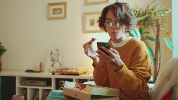 Pozytywna Brunetka Okularach Jedząca Pizzę Pisząca Smsy Komórce Kanapie Domu — Wideo stockowe