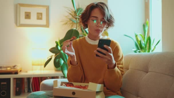 Mulher Morena Confiante Óculos Comendo Pizza Mensagens Texto Telefone Sofá — Vídeo de Stock