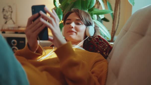 Uśmiechnięta Brunetka Słuchająca Muzyki Słuchawkach Pisząca Telefonie Komórkowym Domu — Wideo stockowe