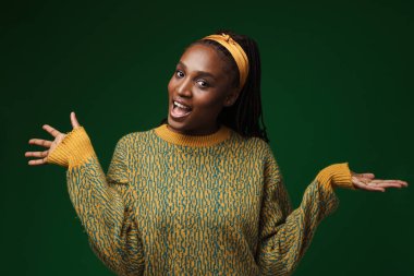 Genç siyahi bir kadın yeşil duvarın üzerinde izole edilmiş kopyalama alanını tutarken gülüyor.