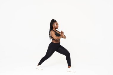 Yoga yaparken poz veren siyah genç bir kadın beyaz arka planda izole edilmiş.