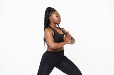 Yoga yaparken poz veren siyah genç bir kadın beyaz arka planda izole edilmiş.