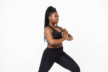 Yoga yaparken poz veren siyah genç bir kadın beyaz arka planda izole edilmiş.