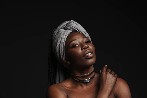 Shirtless black woman wearing headscarf looking at camera isolated over dark background