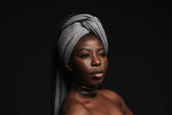 Shirtless black woman wearing headscarf looking aside isolated over dark background
