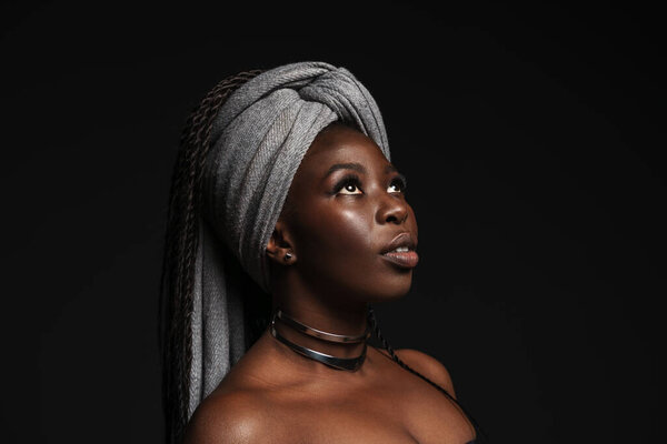 Shirtless black woman wearing headscarf looking downward isolated over dark background