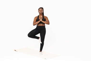 Yoga yaparken poz veren siyah genç bir kadın beyaz arka planda izole edilmiş.