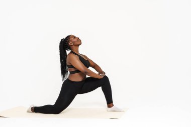 Yoga yaparken poz veren siyah genç bir kadın beyaz arka planda izole edilmiş.