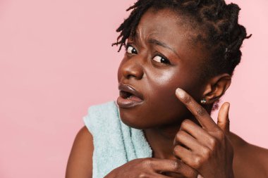 Pembe arka planda, tenine havluyla dokunan siyah hoşnutsuz kadın.