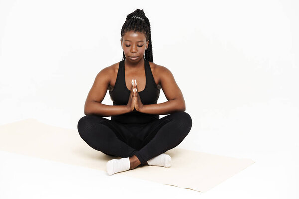 Черная юная спортсменка медитирует во время занятий йогой на белом фоне