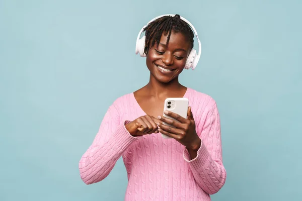 Afroamerikansk Ung Kvinna Ler När Använder Mobiltelefon Och Hörlurar Isolerade — Stockfoto