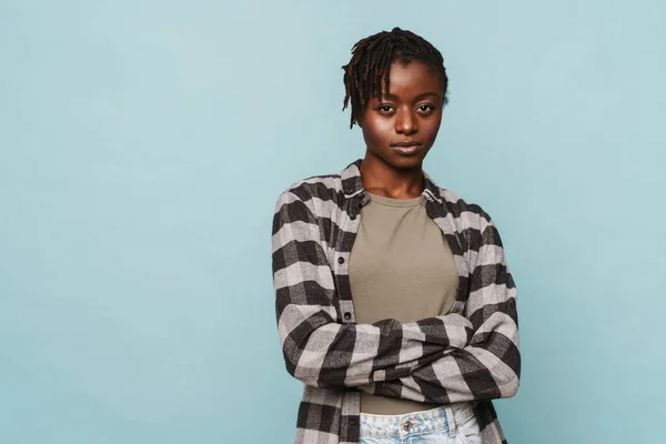 身穿格子呢衬衫的非洲裔美国女青年 双臂交叉 蓝色背景与外界隔绝 — 图库照片