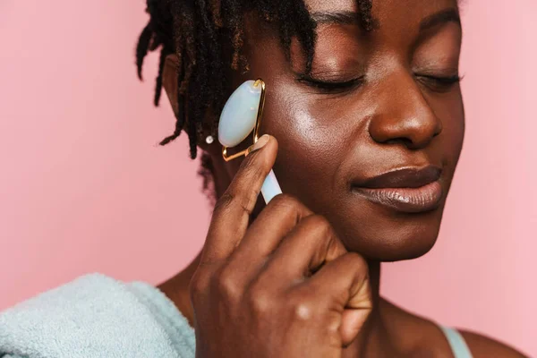 Stock image Black shirtless woman massaging face with jade roller isolated over pink background