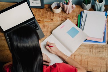 Genç İspanyol kadın evde dizüstü bilgisayarla çalışırken organizatörde notlar yazıyor.