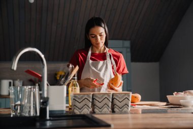 Genç İspanyol kadın mutfakta yemek pişirirken tatlı patates soyuyor.