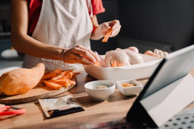 Evde yemek pişirirken tablet bilgisayar kullanan genç bir kadın.