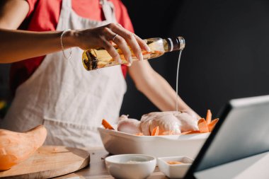 Evde yemek pişirirken tablet bilgisayar kullanan genç bir kadın.