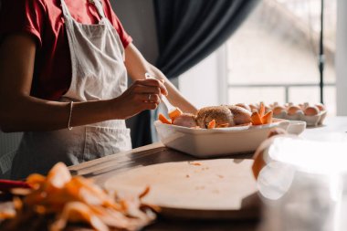 Mutfakta tavuk pişiren önlük giyen genç bir kadın.