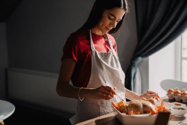 Evde mutfakta önlük giymiş, tavuk pişiren genç İspanyol kadın.