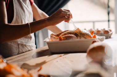 Mutfakta tavuk pişiren önlük giyen genç bir kadın.