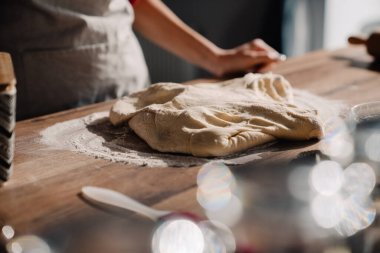 Önlük takan genç bir kadın mutfakta yemek pişirir ve hamur yoğurur.