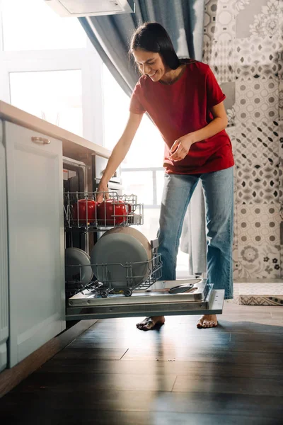 Stock image Young hispanic woman using dishwasher while doing housework at home