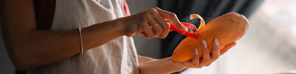 家庭で台所で調理しながら サツマイモを剥離エプロンを身に着けている若い女性 — ストック写真
