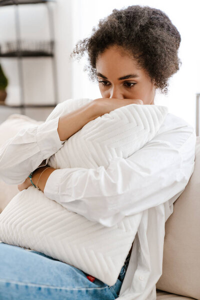 Молодая черная женщина расстроена и думает об аборте, сидя дома на диване