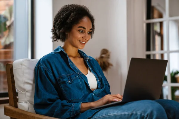 Молода Чорна Жінка Джинсовій Сорочці Посміхається Використовує Ноутбук Вдома — стокове фото