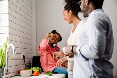 Afrikalı Amerikalı mutlu adam ve küçük kızı olan kadın evde mutfakta kahvaltı hazırlıyorlar.