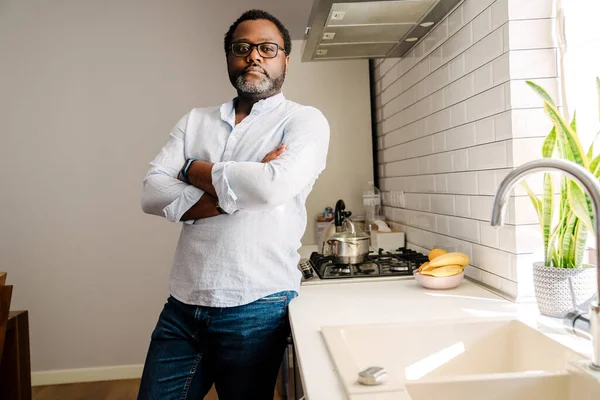 African american adult man wearing eyeglasses standing with arms folded in kitchen