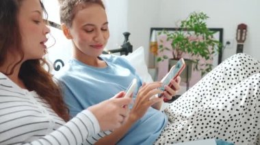 Telefonla yazan ve evde yatakta konuşan mutlu kız arkadaşlar.