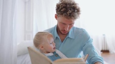Güzel sarışın baba ve kızı evde kitap okuyorlar.
