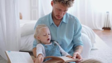 Yakışıklı sarışın baba ve kızı evde kitap okuyor.