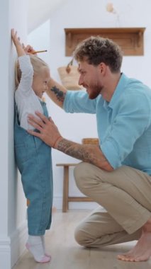 Gülümseyen sarışın baba, kızının boyunu ölçüyor.